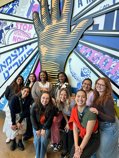 Group of people posing in front of colorful mural depicting a hand