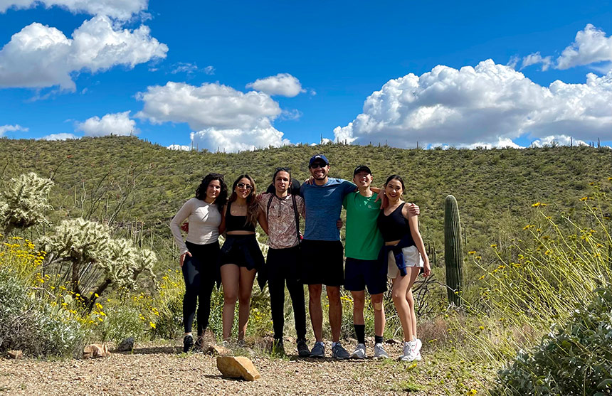 Group of six people posing in desert under blue sky