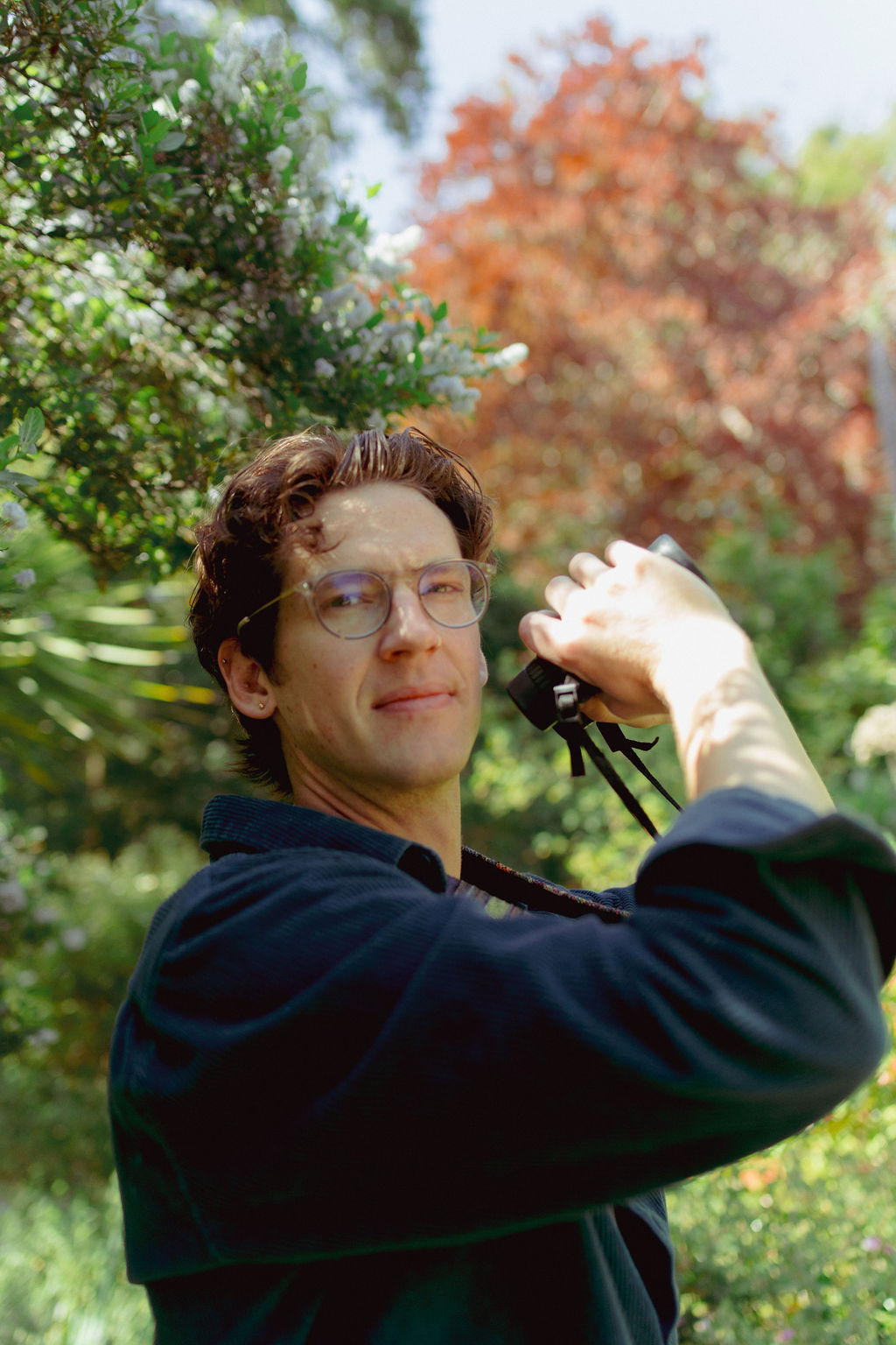 Kevin Steen headshot. Kevin looks at the camera while birdwatching, holding a pair of binoculars. He has a black shirt, medium length curly brown hair, and glasses.