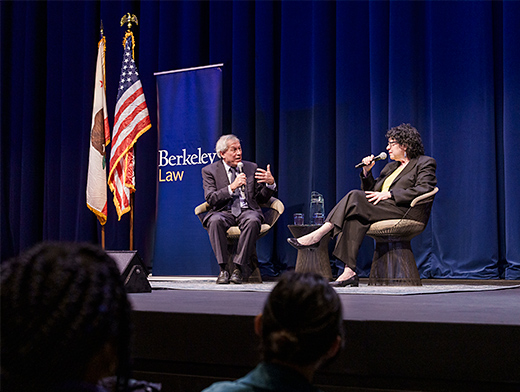 two people seated on stage with microphones